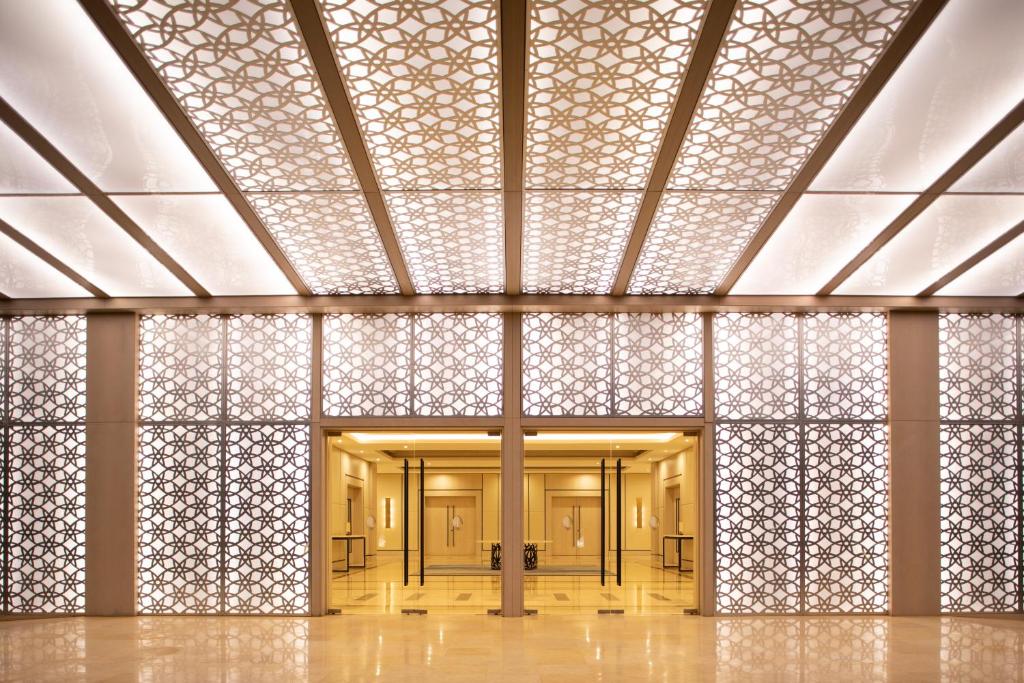 Eleganta interjera ar modernu dizainu, kurā redzami grezni griesti un izsmalcināti apgaismojuma elementi. Telpas centrālajā daļā ir divvērtīgu durvju ieeja, kas vada uz plašu un elegantu telpu.