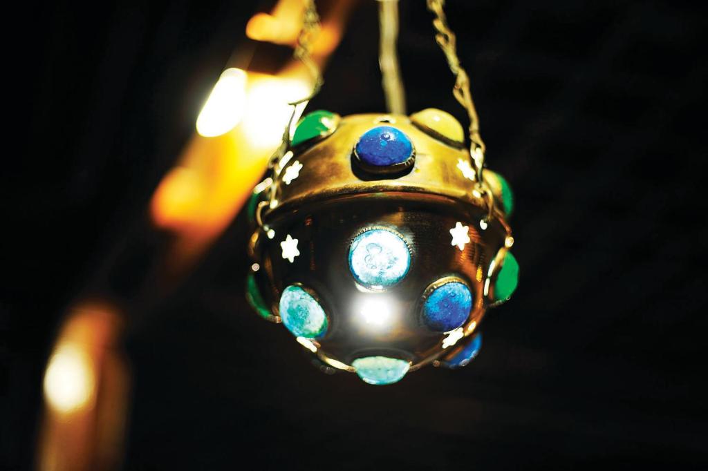 Skaista, dekoratīva lampa ar krāsainiem akmeņiem un zvaigžņu motīviem, kas izstarot siltu gaismu tumšā vidē.