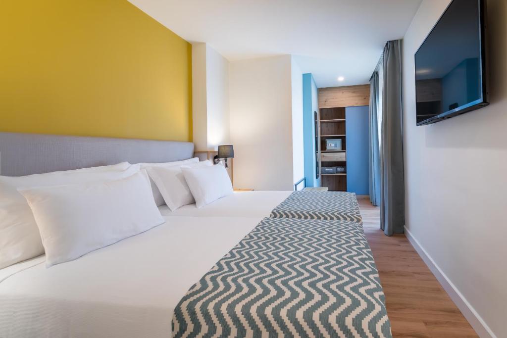 Mūsdienīgs viesnīcas numurs ar divām gultām, gaišām krāsām un dzeltenu akcentu sienā. Telpā ir televizors un virtuvīte, kas pieejama viesu ērtībām.