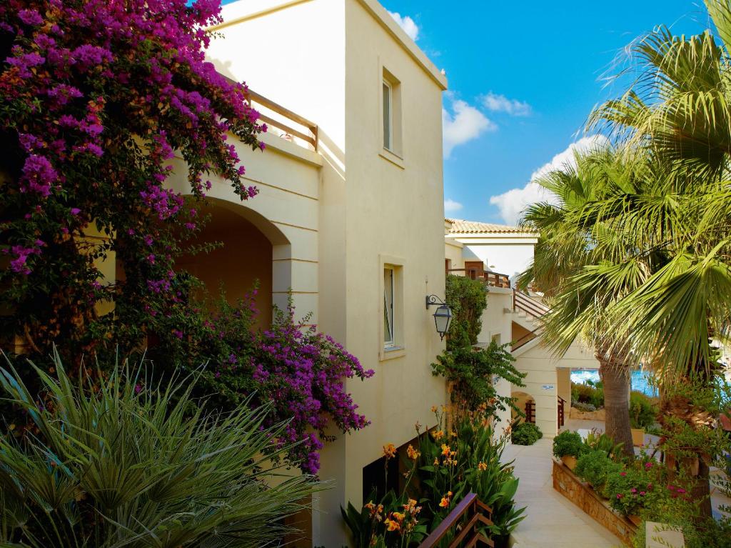 Grecotel Marine Palace & Aqua Park piekrastes ainava ar ziediem un palmām.
