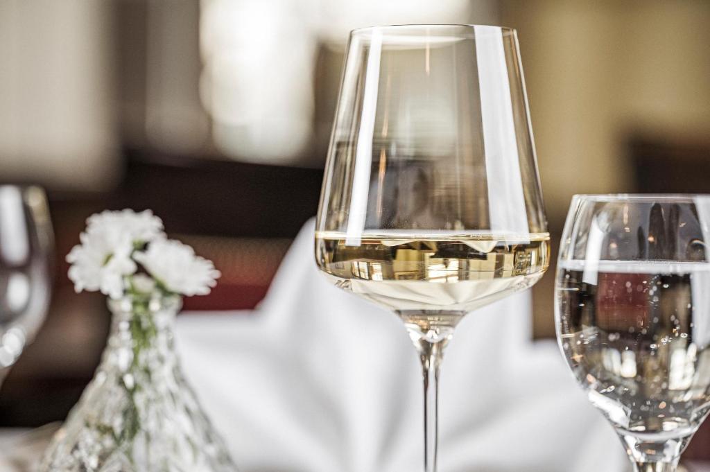 Elegants baltvīna glāze uz galda, blakus glāzei ar ūdeni un nelielai ziedu kompozīcijai. Ideāls attēls, lai izceltu izsmalcinātu ēdienu un dzērienu servēšanu.