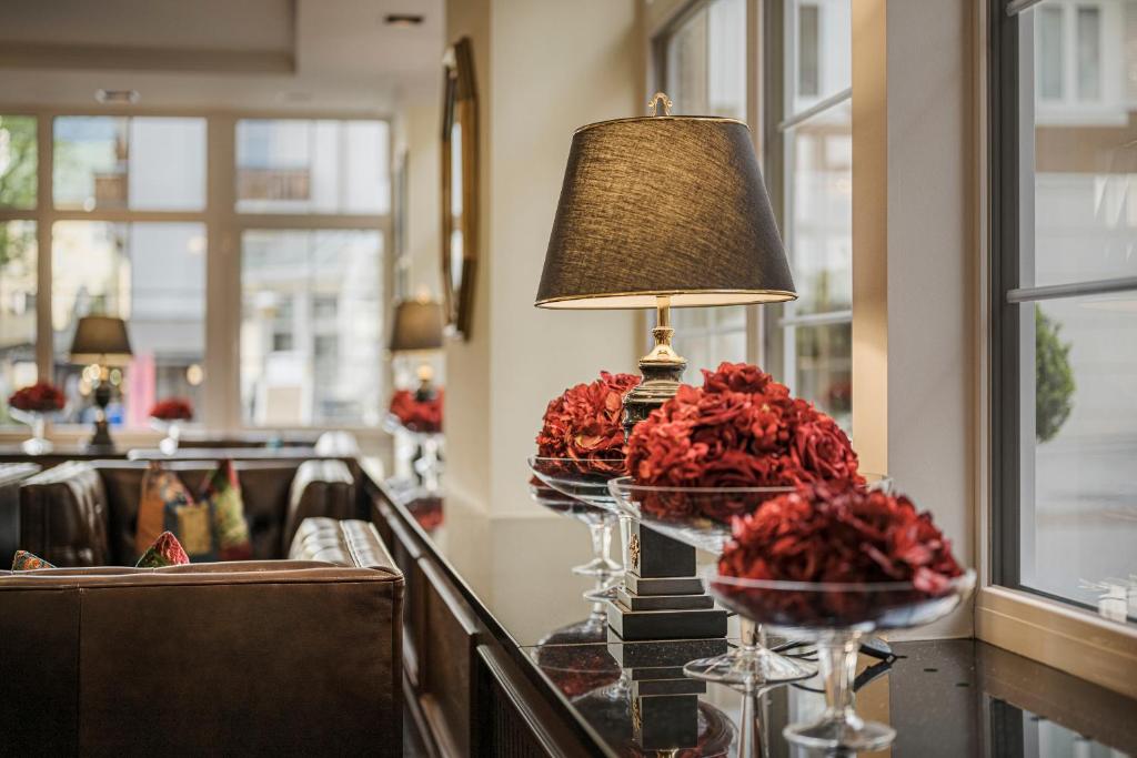 Eleganta viesnīcas interjera aina ar melnu lampu un sarkanu ziedu kompozīcijām uz galda. Gaisma un stilīgs dizains rada mājīgu atmosfēru.