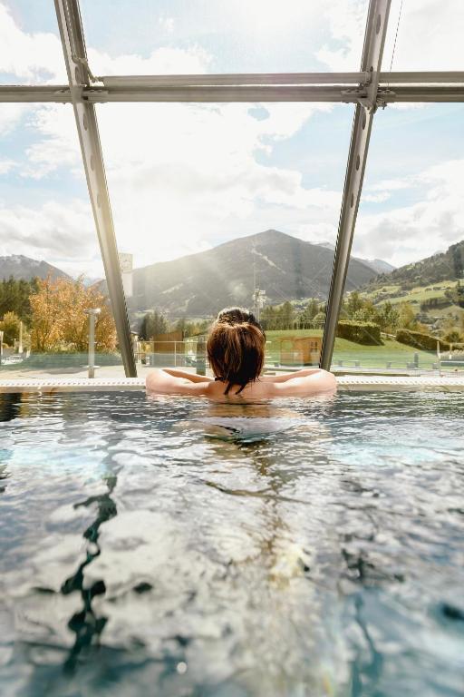 Relaksējoša brīvdiena termālajā baseinā ar skatu uz kalniem, saules gaisma plūst cauri stikla sienām.