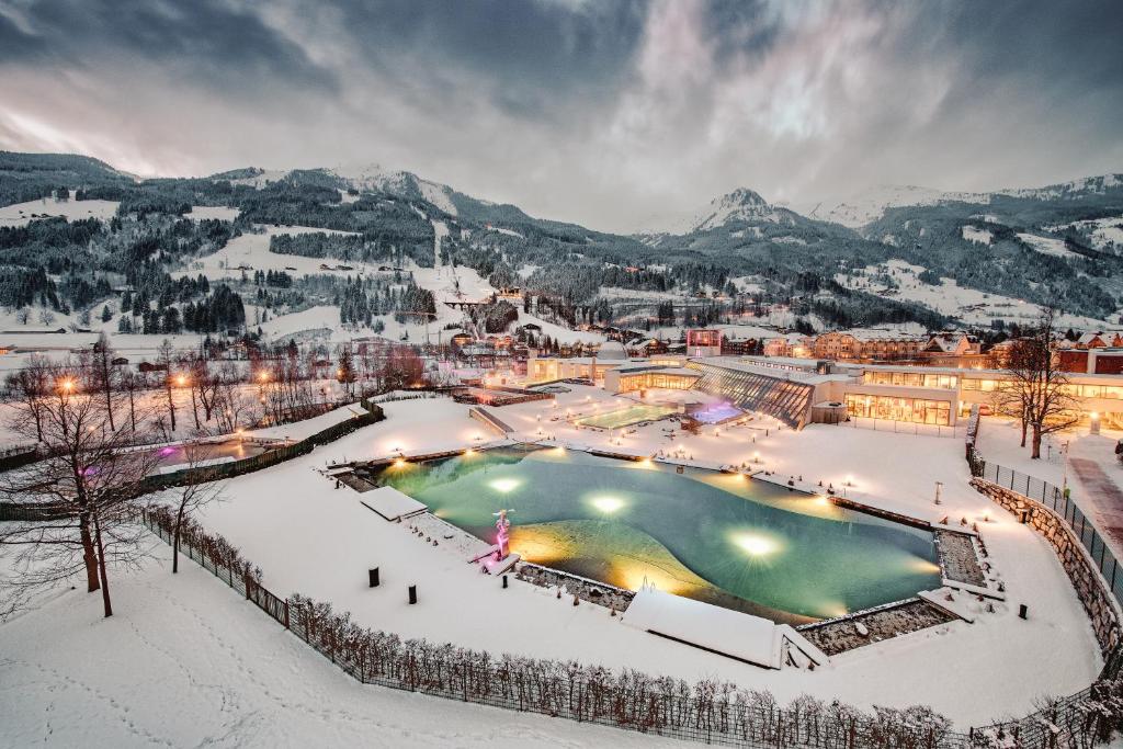 Sniega klātas ainavas skats ar termālo avotu, apgaismotu ar krāsainām gaismām, un kalnu fona. Mierīga ziemas atmosfēra.