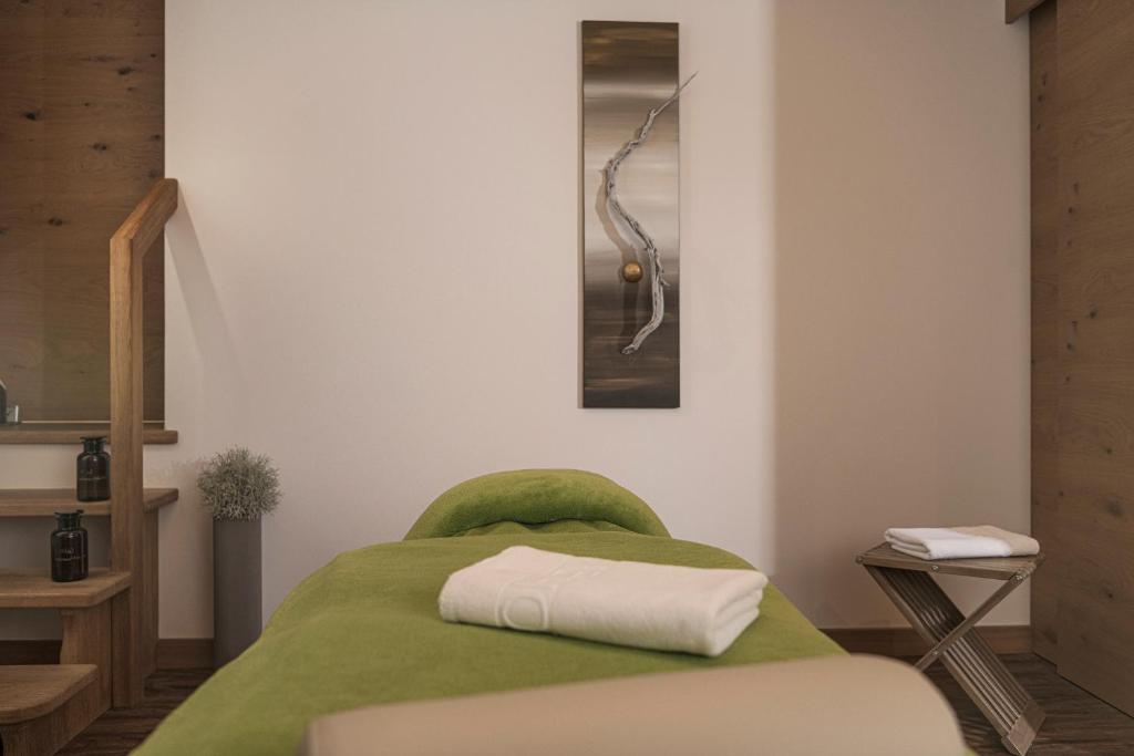 Mierīga spa telpa ar zaļu masāžas galdu, koka kāpnēm un dekoratīvu mākslas darbu uz sienas. Telpa ir gaumīgi iekārtota relaksācijai un atpūtai.