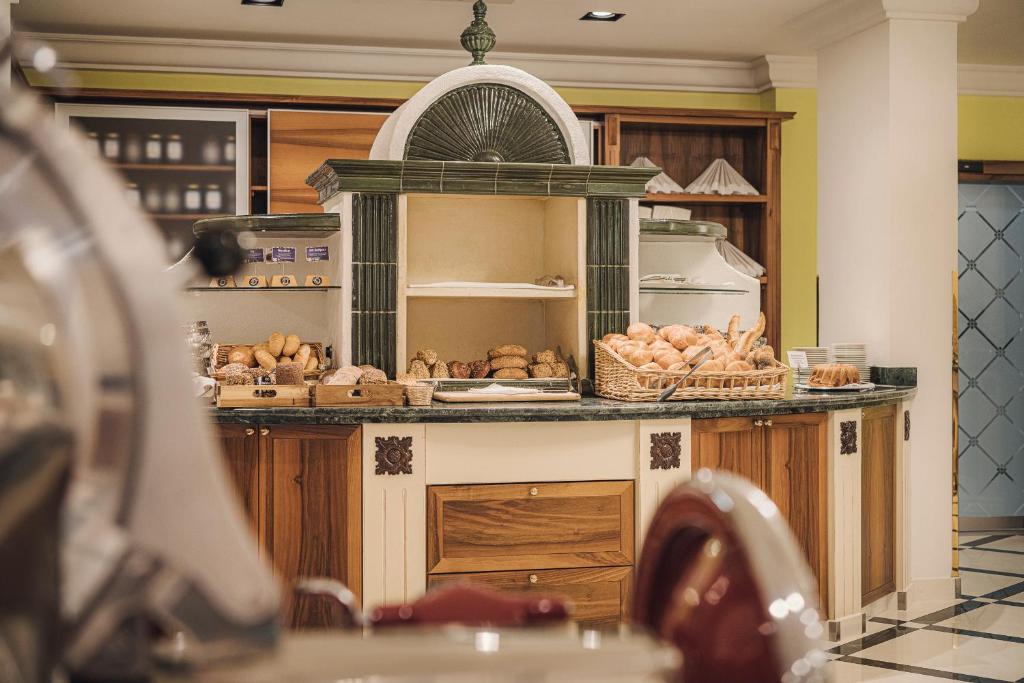 Brokastu bufete ar dažādiem maizes izstrādājumiem, kas sakārtoti elegantā koka skapī. Interjers ir gaišs un moderns, radot patīkamu atmosfēru.