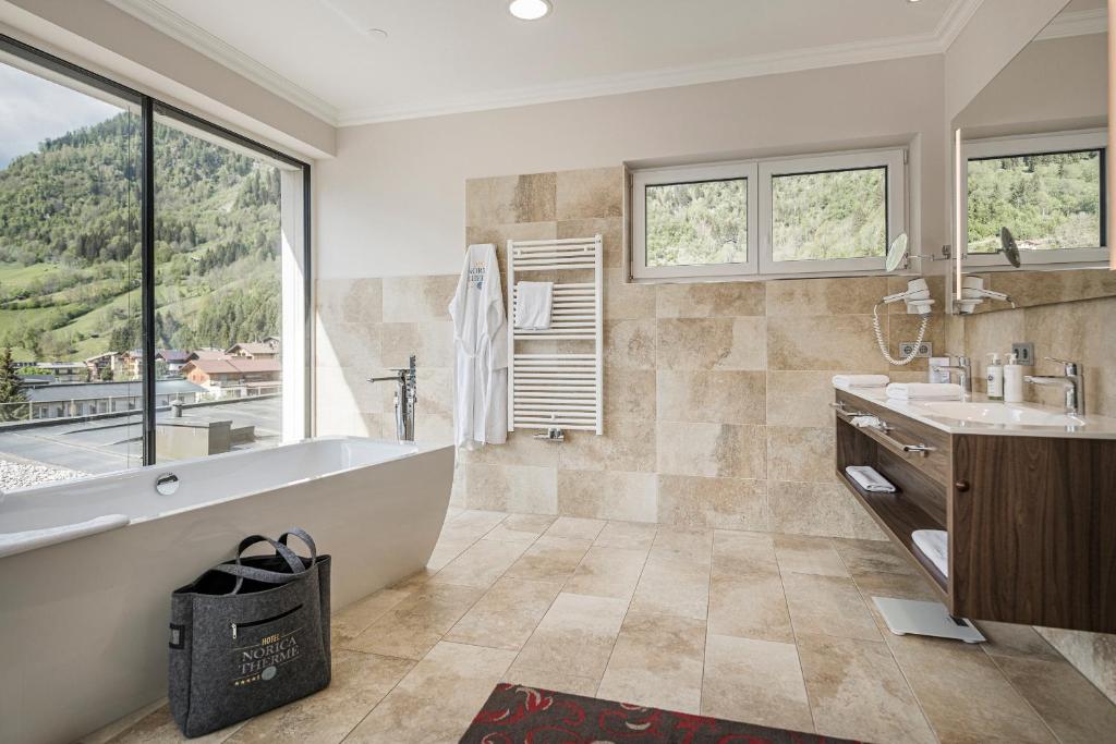 Mūsdienīgs vannas istabas interjers ar lieliem logiem, kas sniedz skatu uz kalniem, elegantu vannu un koka izstrādājumiem. Vannas istabā ir arī dvieļu žāvētājs un izsmalcināti sanitārie piederumi.