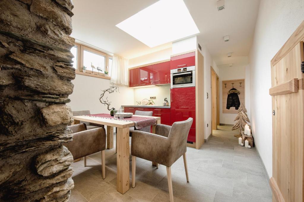 Mūsdienīga virtuve ar sarkanu skapīti un ēdamgaldu, papildināta ar akmens sienu un dabīgu apgaismojumu no jumta loga. Interjers rada siltu un viesmīlīgu atmosfēru.