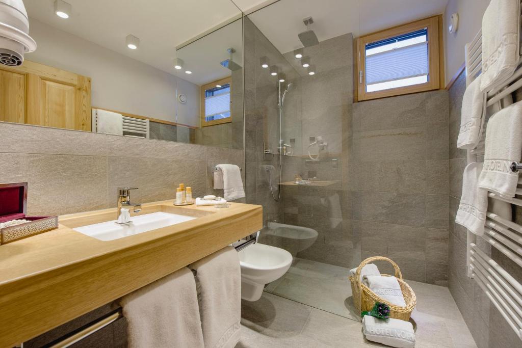 Mūsdienīgs vannas istabas interjers ar koka izlietni, stikla dušu un elegantiem aksesuāriem. Telpa ir gaiša un plaša, ar dabīgā gaismas plūsmu no loga.