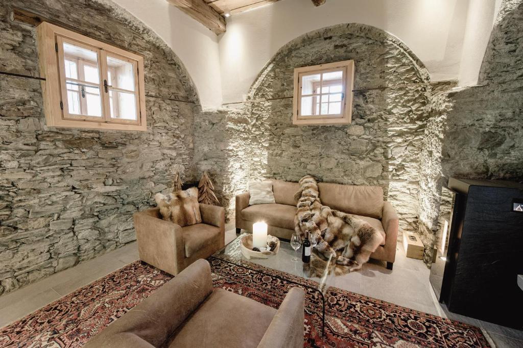 Mūsdienīgs viesistabas interjers ar akmens sienām, ērtiem dīvāniem un elegantu galdu, kas papildināts ar vīna pudelēm un svečturi. Siltas krāsas un tekstūras rada mājīgu atmosfēru.