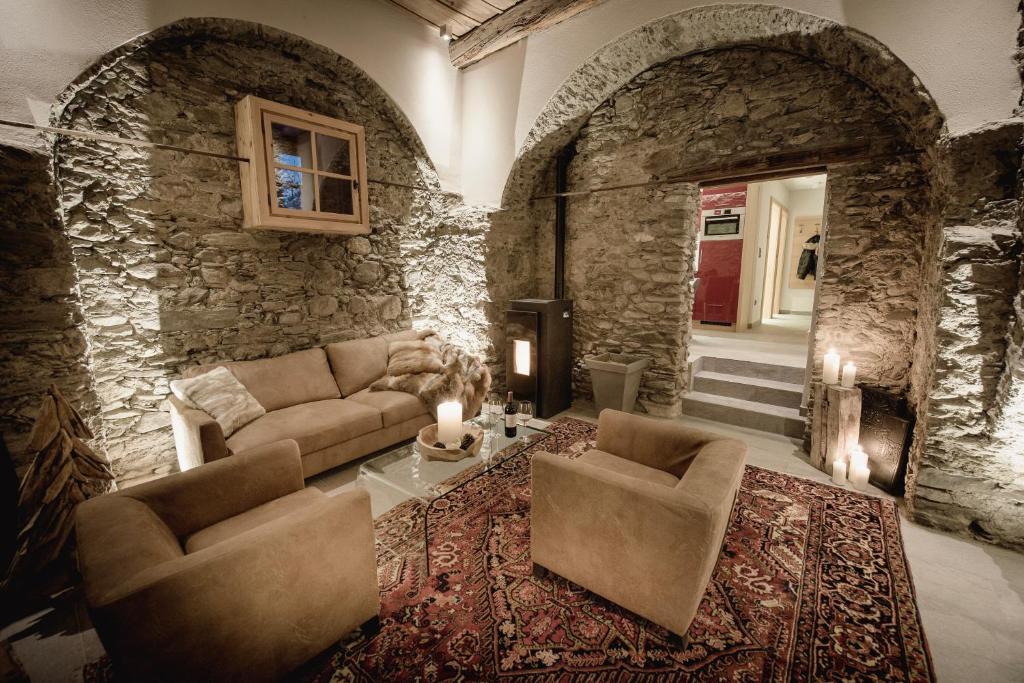 Mūsdienīga viesistaba ar akmens sienām, ērtām dīvāna mēbelēm un siltu apgaismojumu, radot mājīgu un relaksējošu atmosfēru. Elegants paklājs un sveces papildina interjera šarmu.