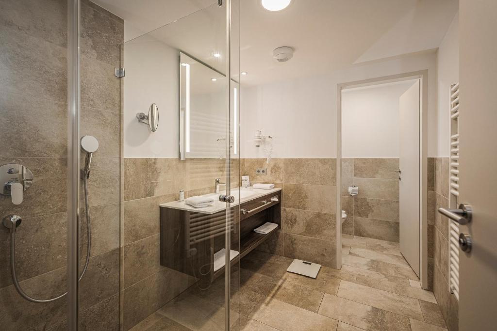 Mūsdienīga vannas istaba ar stikla dušu, elegantu izlietni un akmens flīzēm, kas rada siltu un stilīgu atmosfēru. Vannas istaba ir labi aprīkota ar modernām iekārtām un apgaismojumu.