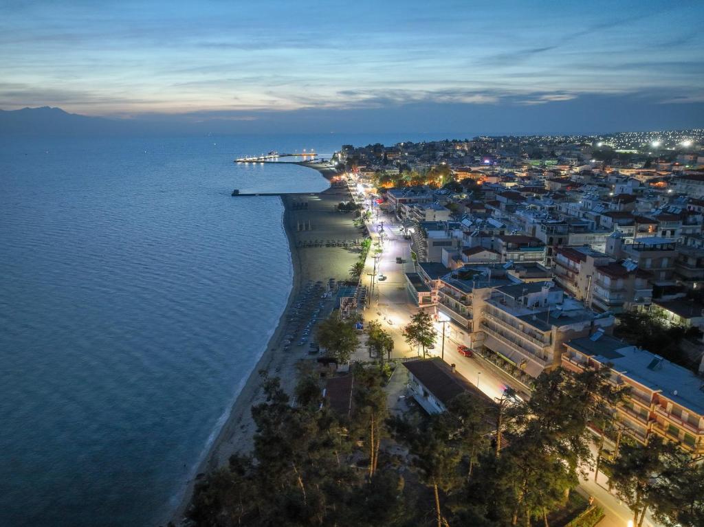 Kūrorts pie jūras, apgaismots vakarā, ar pludmali un ēkām gar krastu. Rāmie ūdeņi un pilsētas gaismas rada mierīgu atmosfēru.