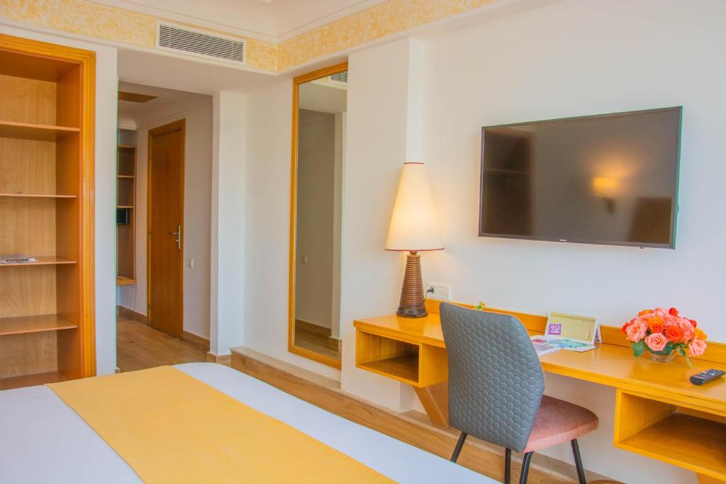 Mūsdienīgs viesnīcas numurs ar ērtu rakstāmgaldu, televizoru un dekoratīvām ziedu kompozīcijām, radot patīkamu atmosfēru. Interjerā dominē gaišas krāsas un koka elementi.