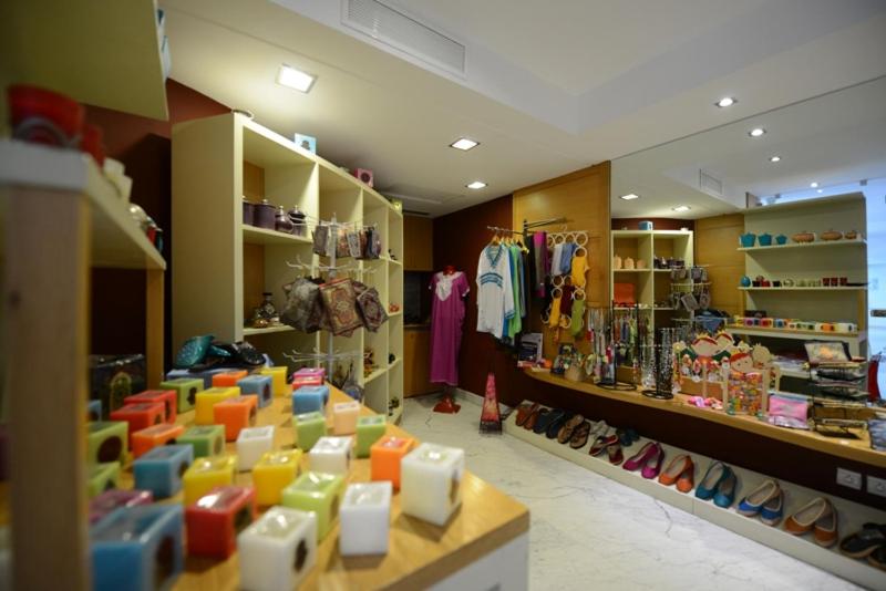 Veikals ar dažādiem izstrādājumiem, ieskaitot apģērbu, aksesuārus un krāsainas sveces, kas izvietoti uz plauktiem un galda. Interjers ir gaišs un mūsdienīgs, radot pievilcīgu iepirkšanās atmosfēru.