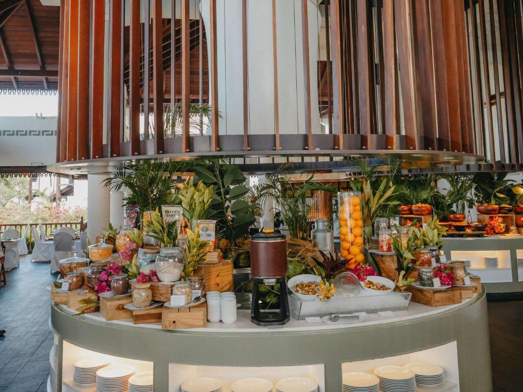 Bagātīgs brokastu bufete ar augļiem, dārzeņiem un dažādiem ēdieniem, izkārtota eleganti ar zaļumiem un rotājumiem. Moderns restorāna dizains ar atvērtu telpu un dabīgu gaismu.