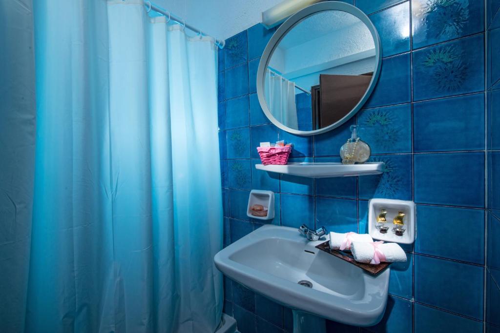 Mūsdienīgs vannas istabas interjers ar zilām flīzēm, apaļu spoguli un higiēnas piederumiem uz plaukta. Gaismas efekts rada patīkamu atmosfēru.