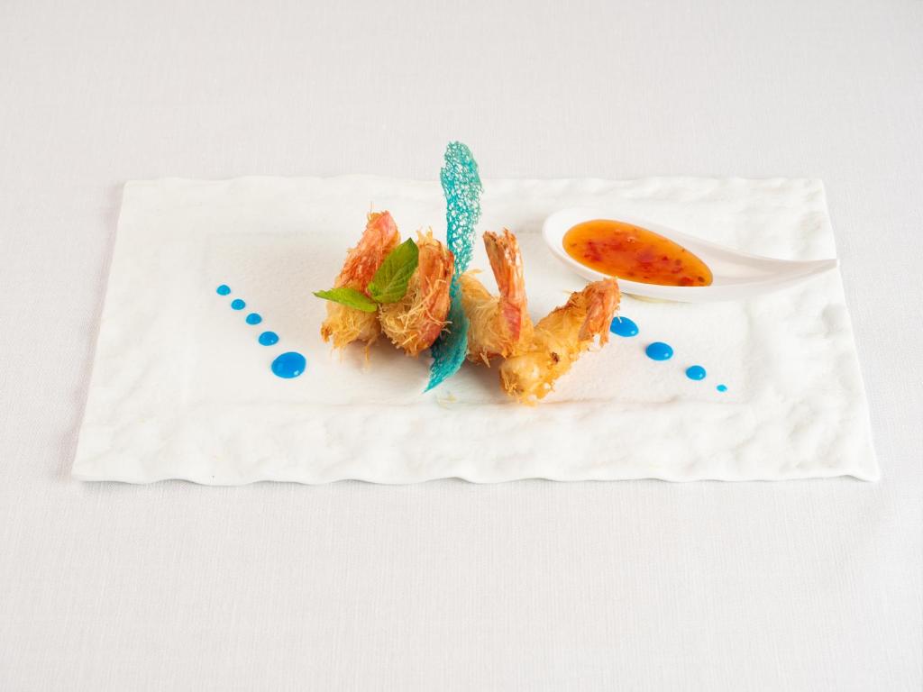 Eleganta ēdiena plate ar kraukšķīgām garnelēm, dekorēta ar zaļām lapām un krāsainu mērci.