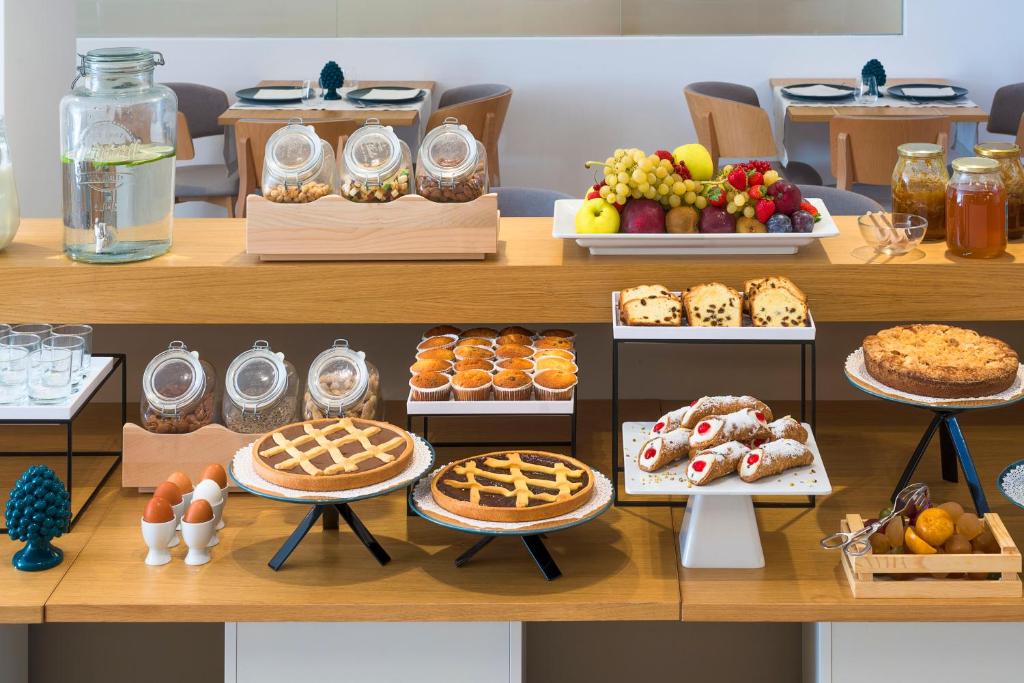 Pusdienu galds ar dažādām kūkām, augļiem un uzkodām, ieskaitot cepumus un riekstu burkas. Svaiga ūdens trauks un deserta dēlis papildina viesmīlīgo atmosfēru.