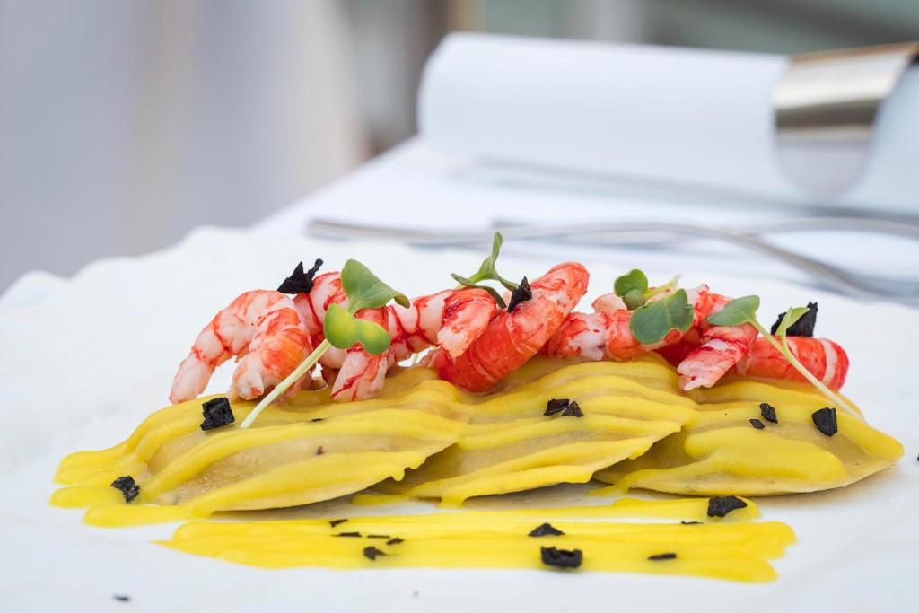Krevetes, kas pasniegti ar dzelteniem ravioli un melniem trifeļu gabaliņiem, dekorēti ar zaļumiem un mērci.