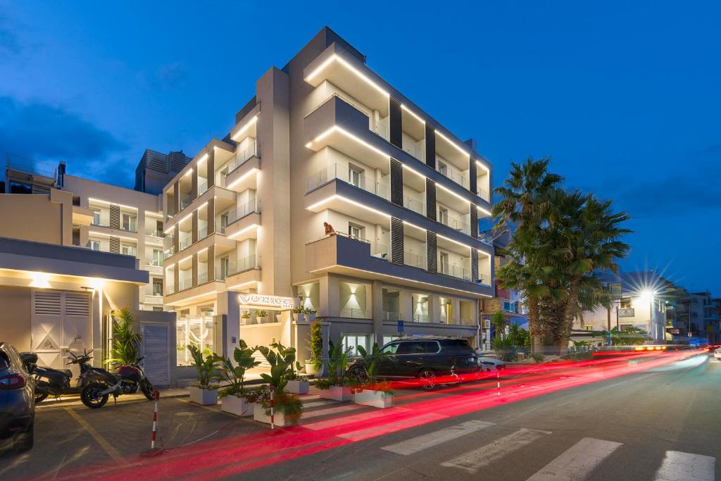 Moderns viesnīcas ēka ar apgaismojumu, kas izceļ tās arhitektūru, un palmām priekšā, atrodas pilsētas ielā pie krēslas.