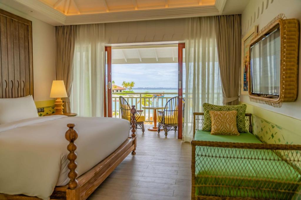 Gaisīgs viesnīcas numurs ar skatu uz jūru, ietver komfortablu gultu, elegantu mēbelējumu un plašas durvis uz balkonu. Iekārtojums rada relaksējošu atmosfēru.