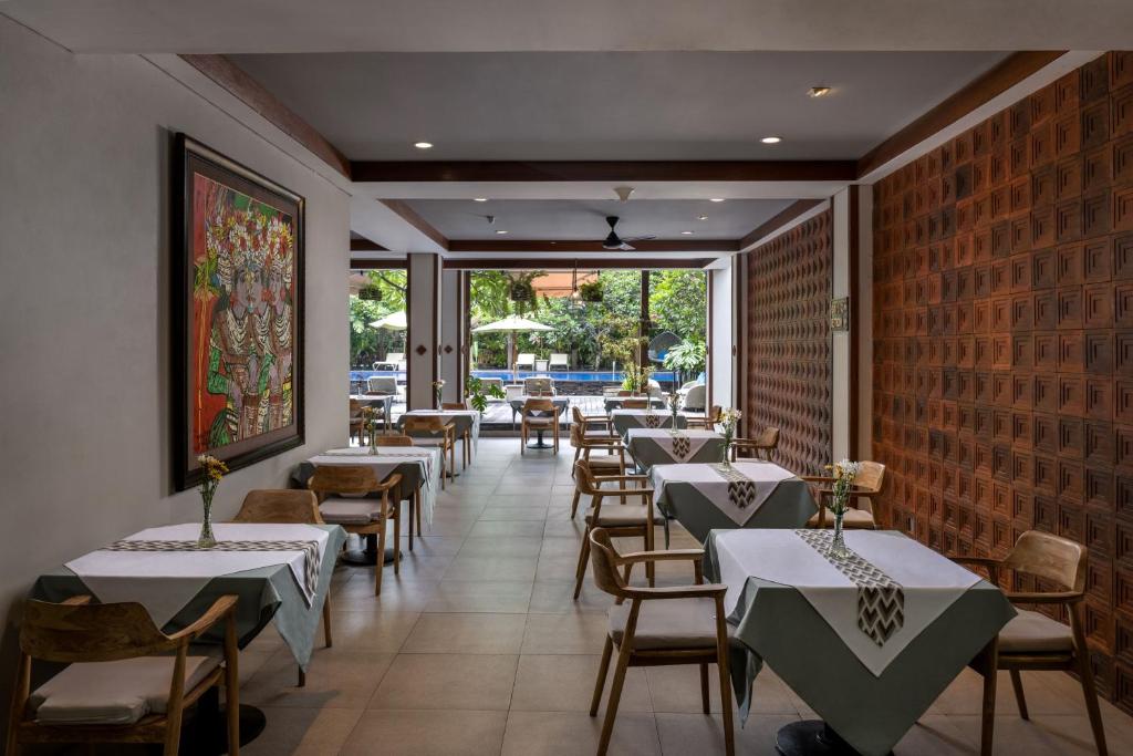 Taksu Hotel Sanur elegantā restorāna interjers ar galdiem un zaļumiem
