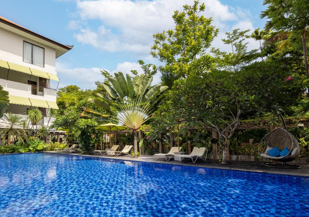Taksu Hotel Sanur baseins ar saulessargiem un tropu augiem.