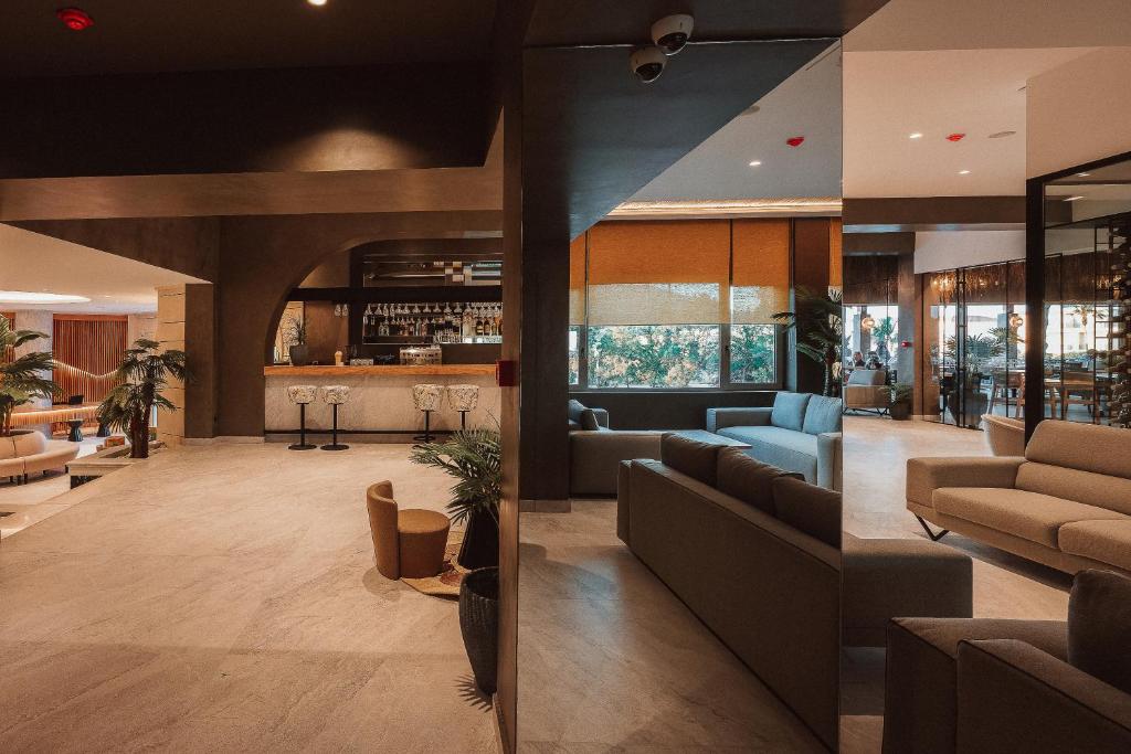 Mūsdienīgs viesnīcas interjers ar stilīgu bāru, ērtām dīvānu zonām un augiem, kas piešķir dzīvīgumu. Telpa ir gaiša un plaša, radot patīkamu atmosfēru.