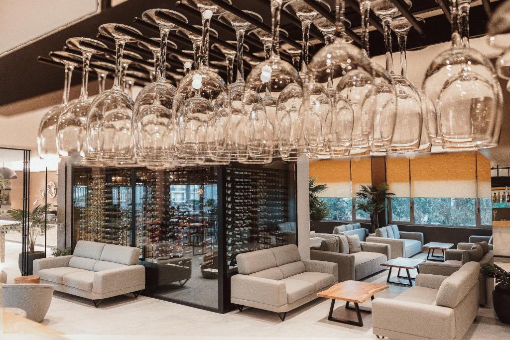 Elegants interjers ar pelēkām dīvānu grupām un glīti sakārtotiem vīna glāzēm, kas karājas no griestiem. Telpa ir apgaismota ar dabīgu gaismu, radot patīkamu atmosfēru.