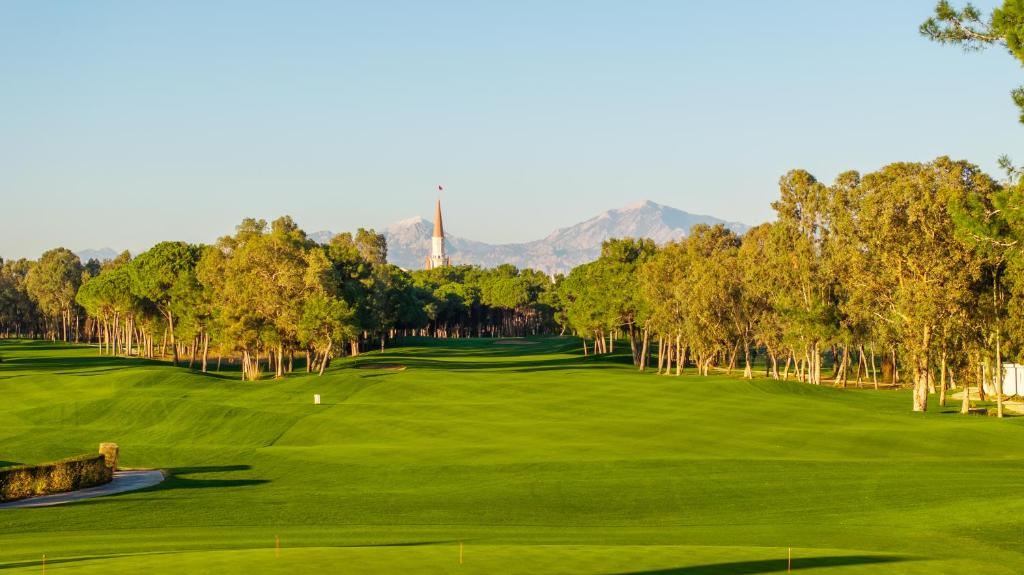 Golf laukums pie Kaya Belek, ar kalniem fonā un košām zaļajām pļavām.