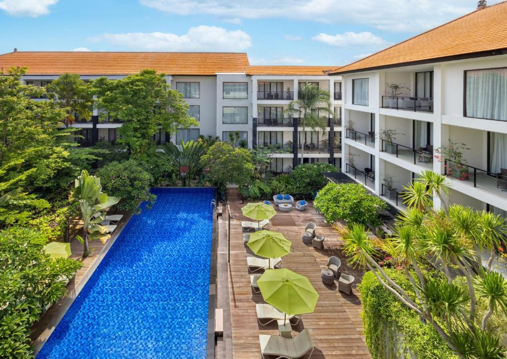 Taksu Hotel Sanur baseins ar saulessargiem un zaļām augiem