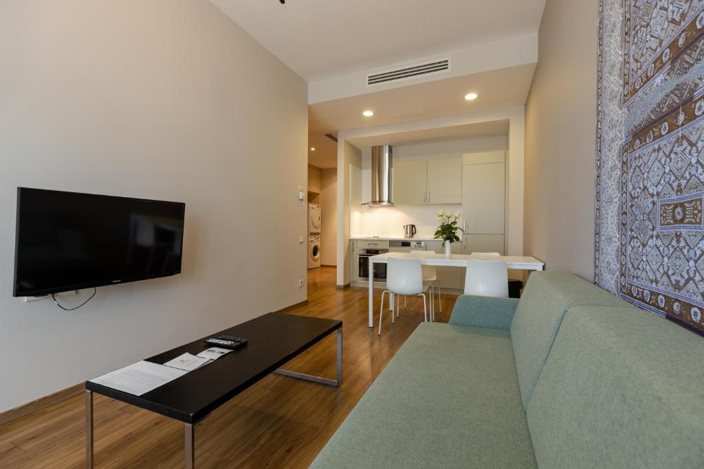 Mūsdienīga viesnīcas numura iekārtojums ar viesistabu, virtuvi un elegantu dekoru. Telpā ir televizors, dīvāns un galda zona.