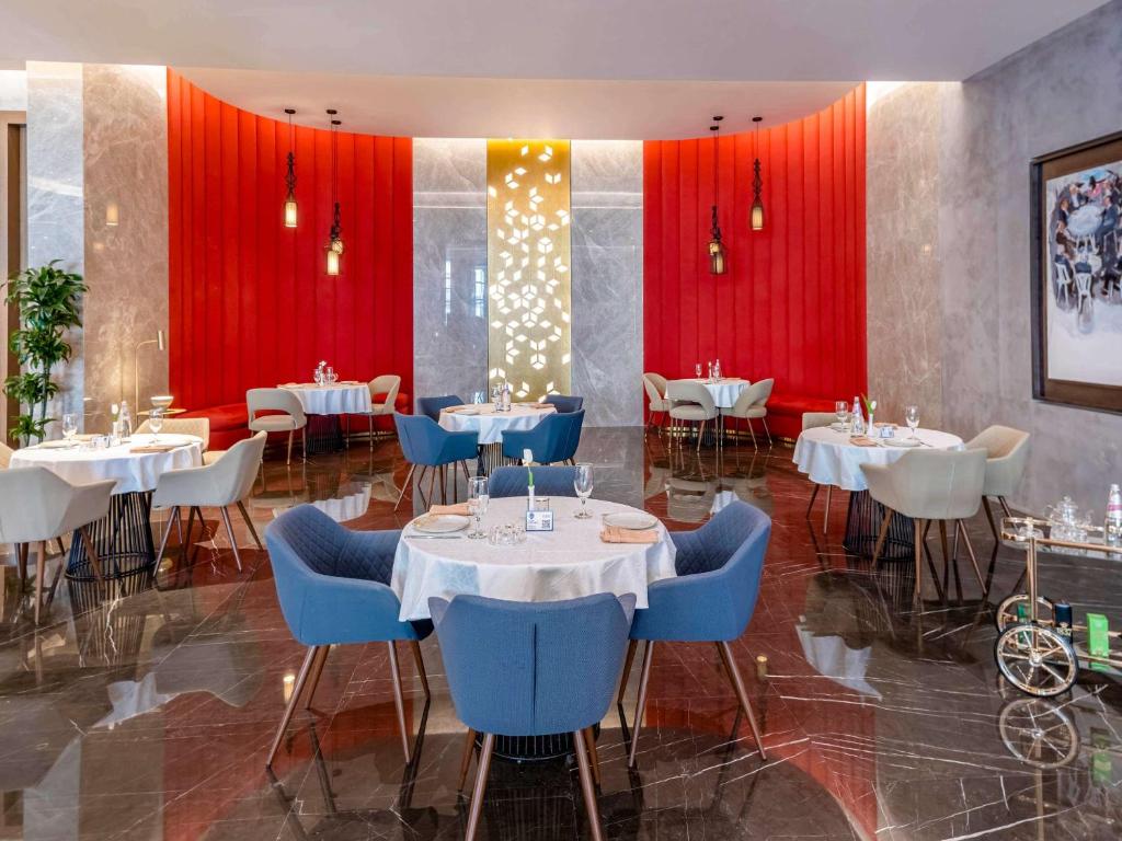 Elegants restorāns ar moderna interjera dizainu, kurā redzami apaļi galdi, stilīgas krēsli un krāsaini akcenti. Sienas rotā spilgti sarkani toņi un dekoratīvi elementi, radot patīkamu atmosfēru.