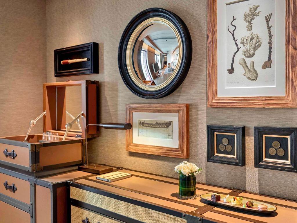 Mūsdienīgs interjers ar elegantiem dekoratīviem elementiem, ieskaitot spoguli, rāmjus ar mākslas darbiem un stilīgu uzglabāšanas sistēmu. Uz galda atrodas dažādi uzkodu grozi un ziedu kompozīcija.