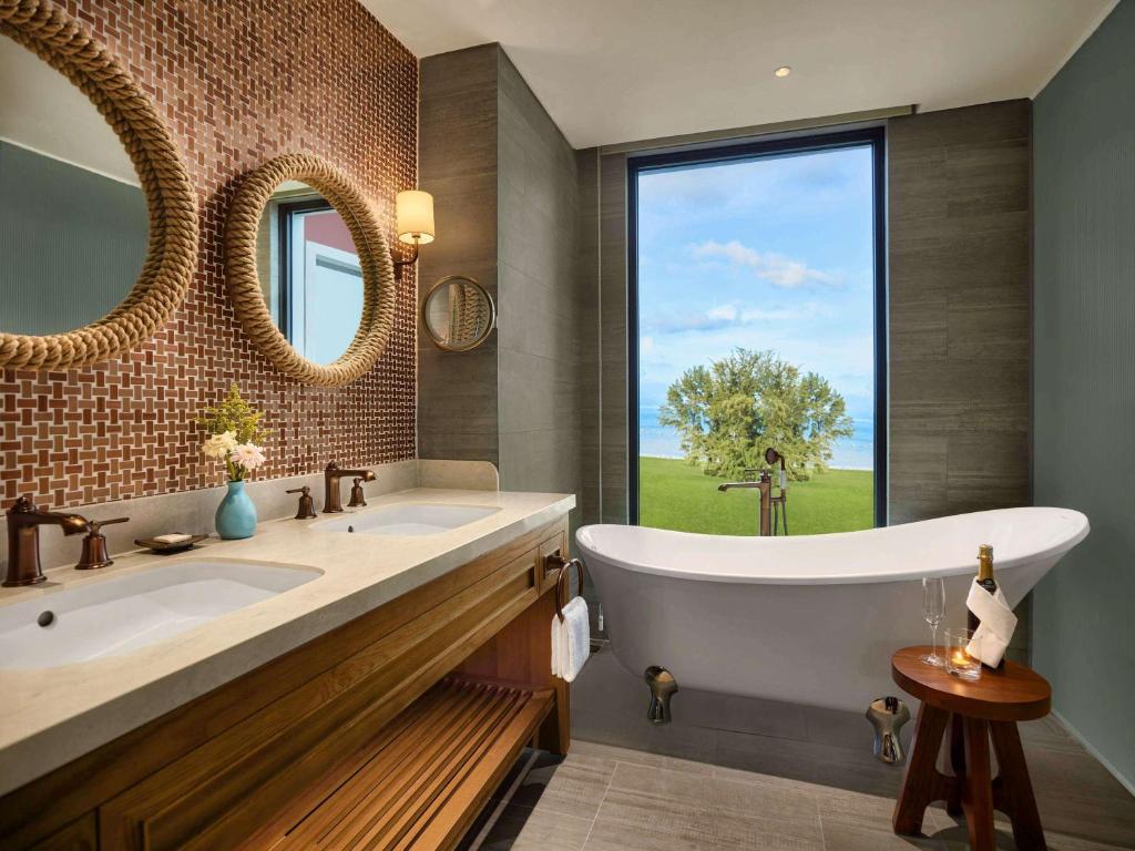 Moderns vannas istabas dizains ar divām izlietnēm, lielu vannu un logu, kas paver skatu uz dārzu. Interjerā ir izmantoti dabīgi materiāli un siltas krāsas, radot relaksējošu atmosfēru.