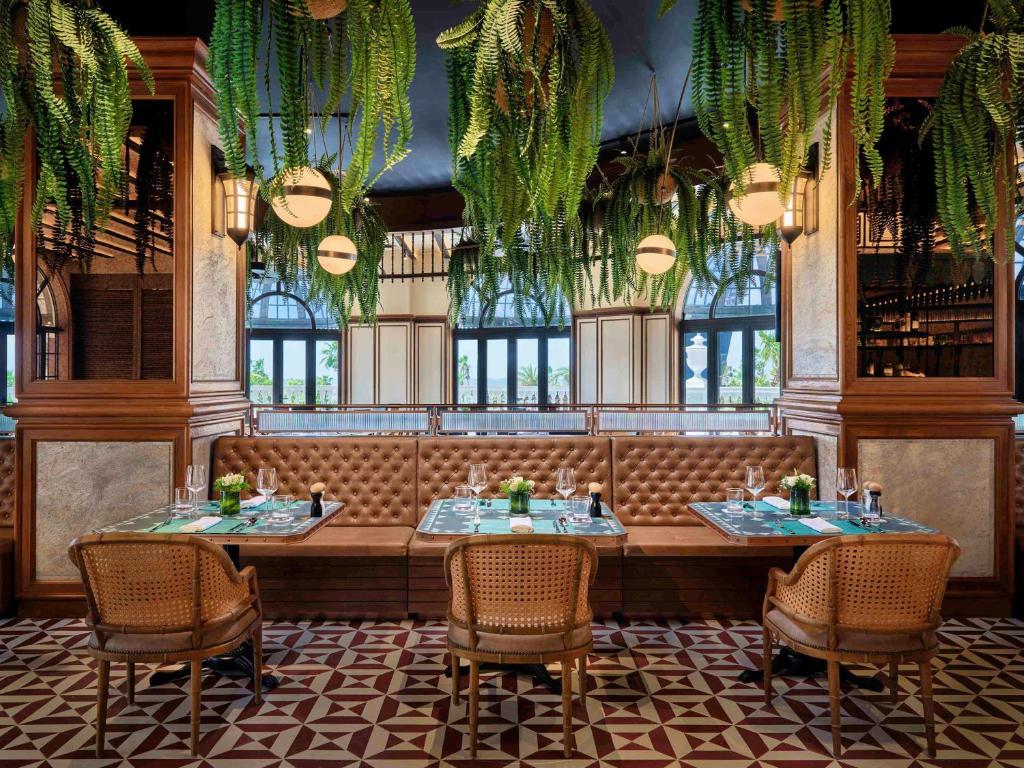 Elegants restorāns ar zaļām lapām pie griestiem, koka elementiem un mājīgām sēdvietām. Interjers izceļas ar modernu stilu un siltu atmosfēru.