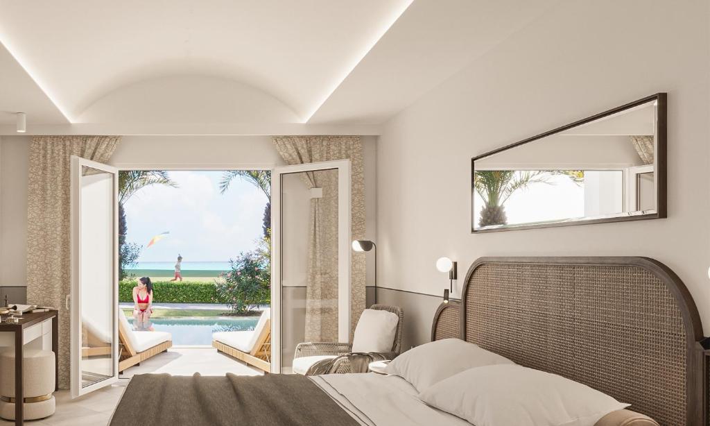 Mūsdienīga guļamistaba ar skatu uz pludmali, kur atvērti balkona durvis ļauj ienākt saules gaismai. Telpā ir komfortabla gulta un relaksācijas zona ar sauļošanās krēsliem.