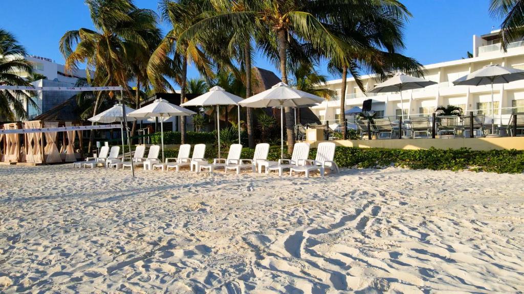 Atpūtas krēsli pie Cancun Bay Resort pludmalē, zem saules jumtiem.