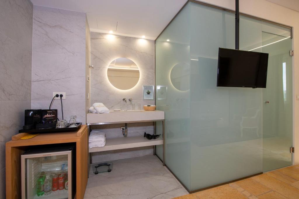 Mūsdienīgs vannas istabas interjers ar stikla sienām, plūstošu gaismu un TV. Uz galda pieejama kafijas automāts un mini ledusskapis.