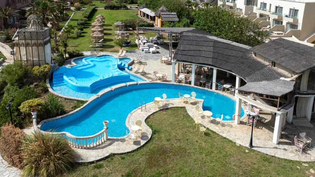 Peldbaseins ar unikālu formu un apkārtējā dārza zona, kurā ir saulessargi un atpūtas vietas, piedāvā relaksējošu atmosfēru. Apkārtnē redzama arī ēdamzona ar galdiem un krēsliem.