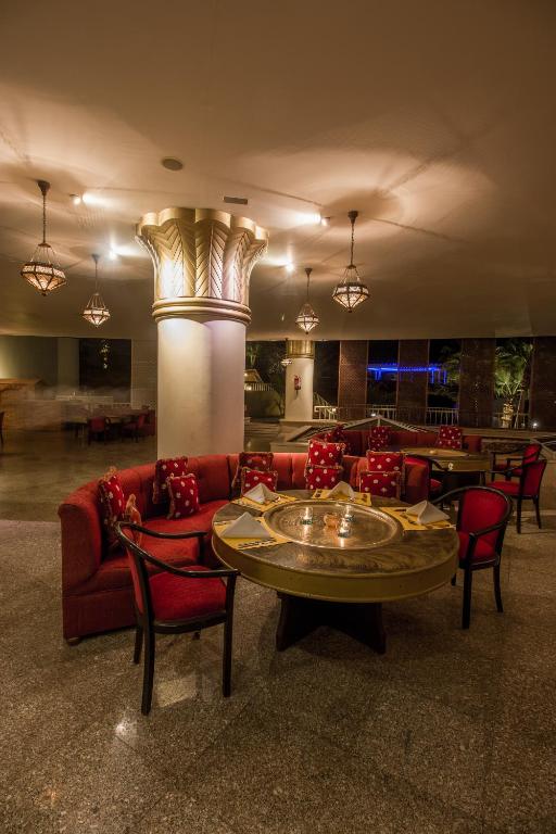 Elegantā interjera restorāns ar sarkaniem dīvāniem un apgaismojumu, radot patīkamu atmosfēru. Centrā atrodas apaļš galds ar svečturi, kas piešķir papildus šarmu.