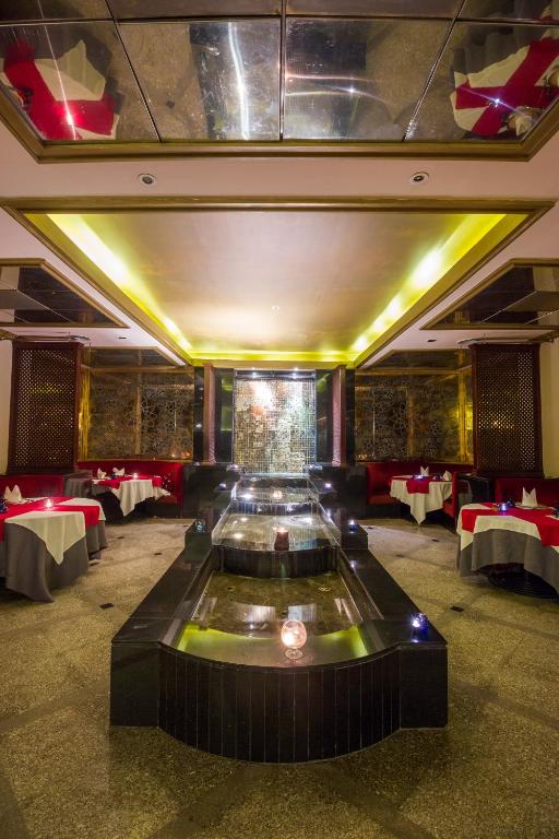 Eleganta restorāna interjers ar apgaismotiem galdiem un ūdens strūklaku centrā. Sarkanās un pelēkās krāsās veidotās detaļas piešķir atmosfēru.