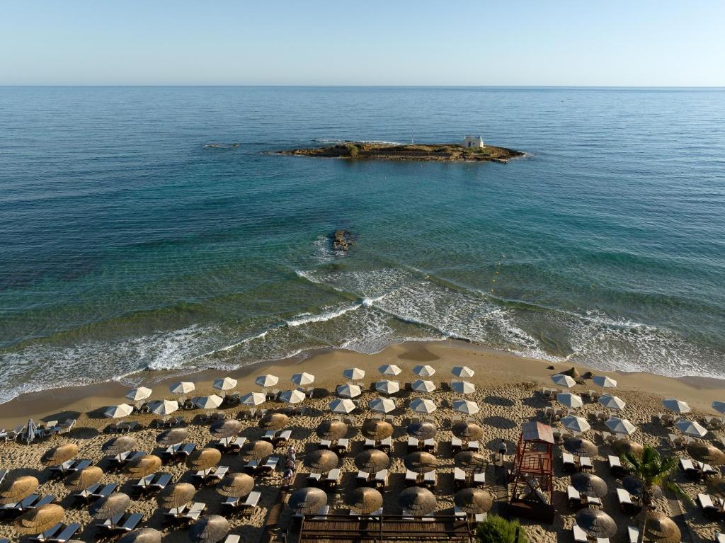 Pludmale ar saulessargiem un šūpuļtīkliem, kas atrodas blakus mierīgai jūrai un nelielai saliņai. Skaists skats uz saulainu laiku un mierīgu okeāna virsmu.