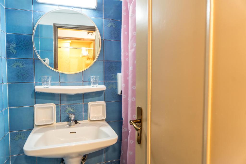 Vannas istaba ar zilu flīžu sienām, apaļu spoguli un izlietni. Uz plaukta atrodas divi glāzes.