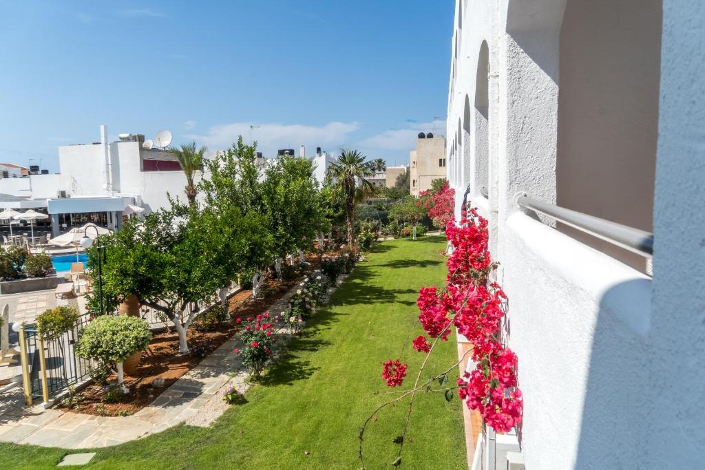 Zaļš dārzs ar ziediem un palmām, redzams no viesnīcas balkona, ar baseina un restorāna ēku fonā.