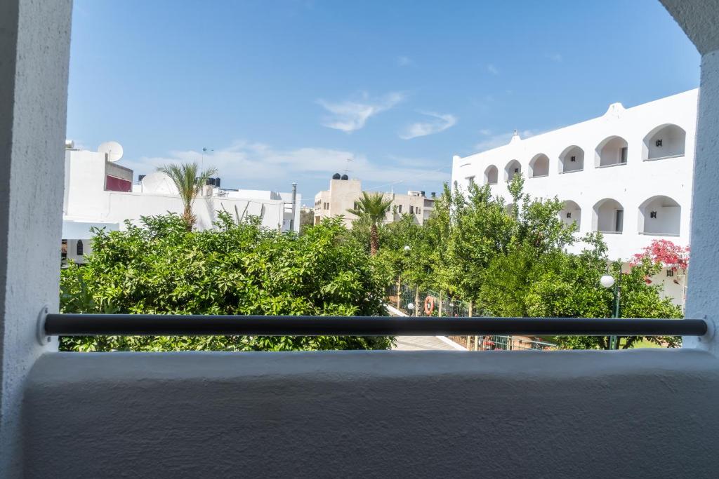 Skats no balkona uz zaļo dārzu un apkārtējām ēkām, skaidra debesis un saulains laiks.