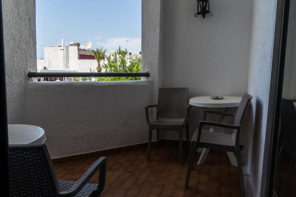 Balkons ar divām krēslām un galdu, kas piedāvā skatu uz zaļām palmām un ēkām. Ideāla vieta relaksācijai un atpūtai.