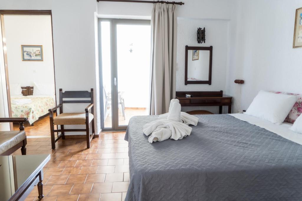 Gaiša viesnīcas istaba ar divguļamo gultu, mīksto dīvānu un balkonu. Telpā redzama eleganta apdare ar flīžu grīdu un koka mēbelēm.