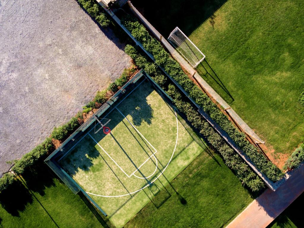 Būvēts sporta laukums ar basketbola un futbola laukumiem, apzaļumots ar zāli un dzīvžogiem, no augšas redzams.